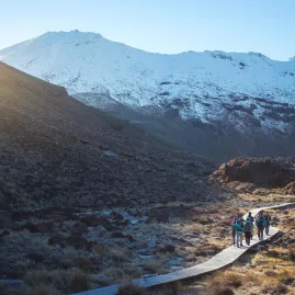 Hikers walking along a snow-dusted boardwalk with Ruapehu and Ngauruhoe in the background