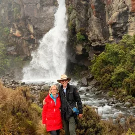 Smiling couple posing by the roaring cascade of Taranaki Falls in Tongariro