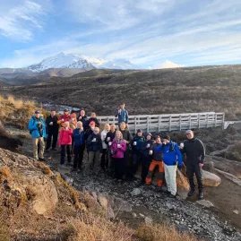 Tour group gathered on a bridge with Mount Ruapehu in the distance on the Taranaki Falls Track
