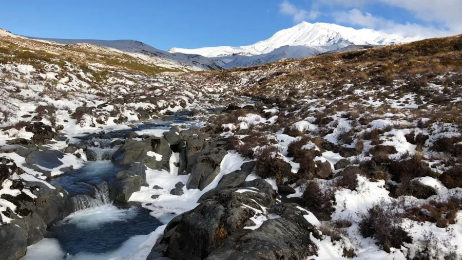 Icy mountain stream flowing beneath a snow-covered Mount Ruapehu in Tongariro National Park