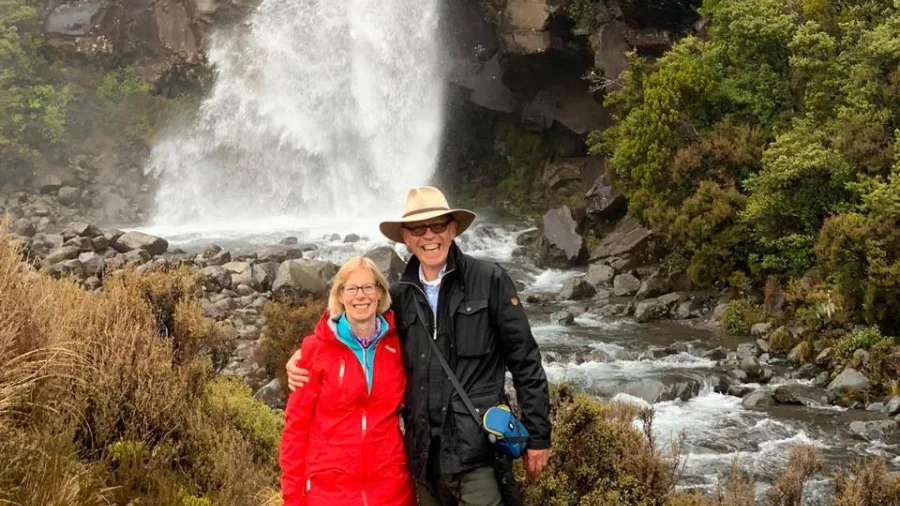 Smiling couple posing by the roaring cascade of Taranaki Falls in Tongariro
