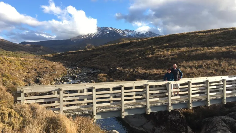 Couple standing on a bridge over an alpine stream with Mount Ruapehu in the distance
