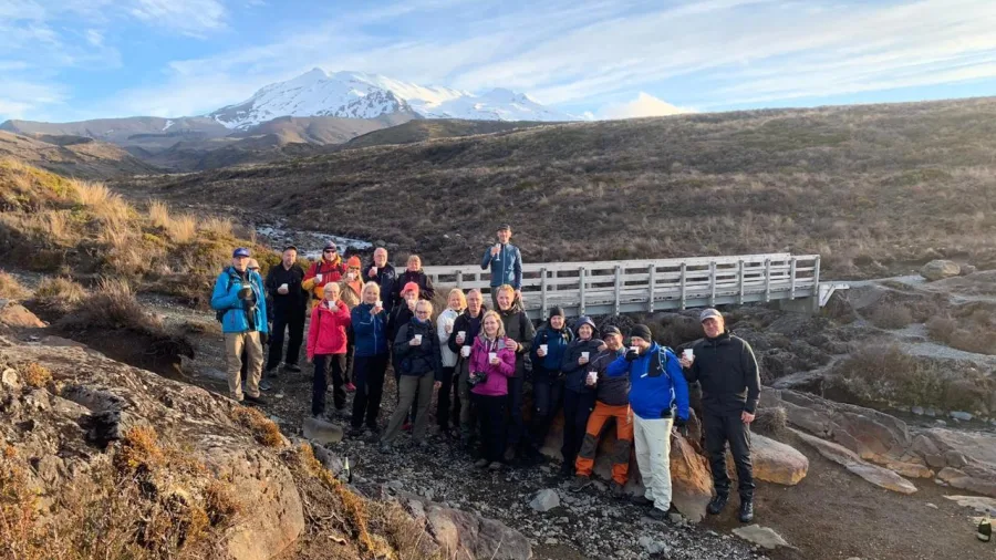 Tour group gathered on a bridge with Mount Ruapehu in the distance on the Taranaki Falls Track