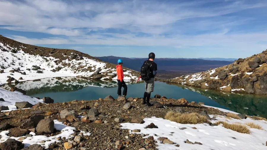 Hikers standing beside an alpine lake with snow patches on Tongariro