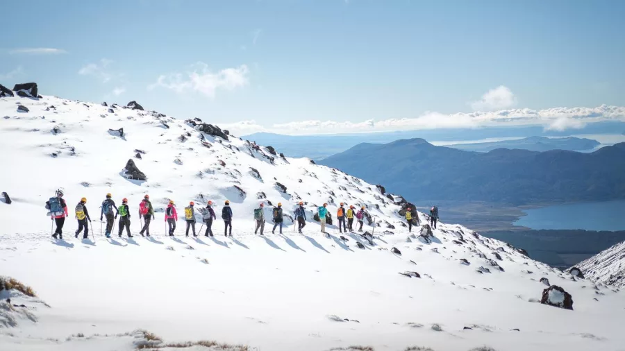 Group of hikers walking in a line through snow on Tongariro Alpine Crossing