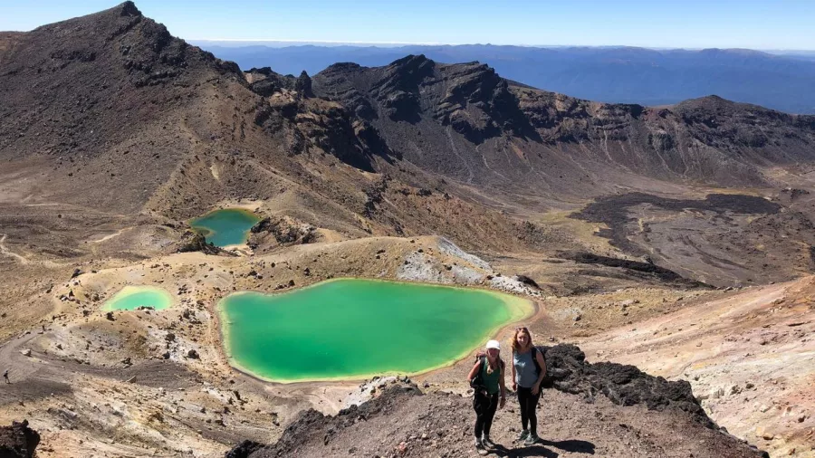 Two women hiking above the Emerald Lakes on the Tongariro Alpine Crossing in summer