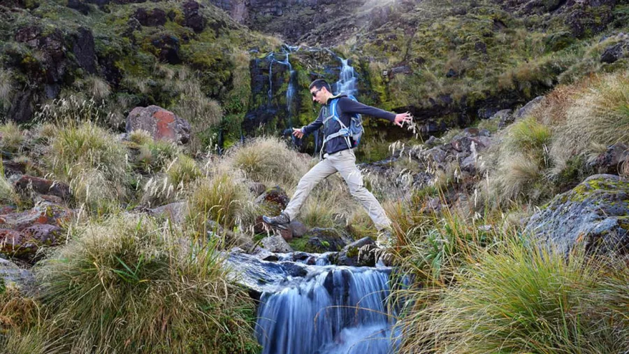 Hiker crossing a small stream below a waterfall on the Tongariro Crossing