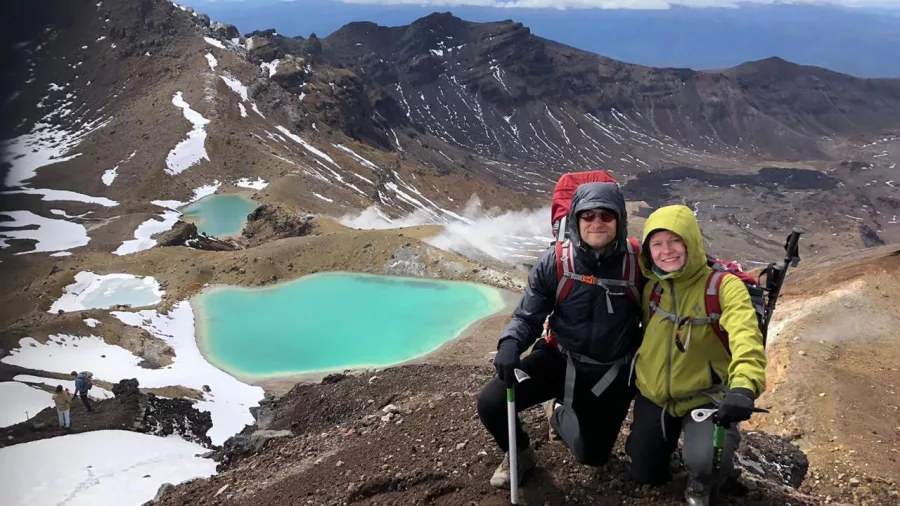 Smiling couple posing with trekking poles above the Emerald Lakes during a winter guided walk
