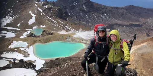 Smiling couple posing with trekking poles above the Emerald Lakes during a winter guided walk