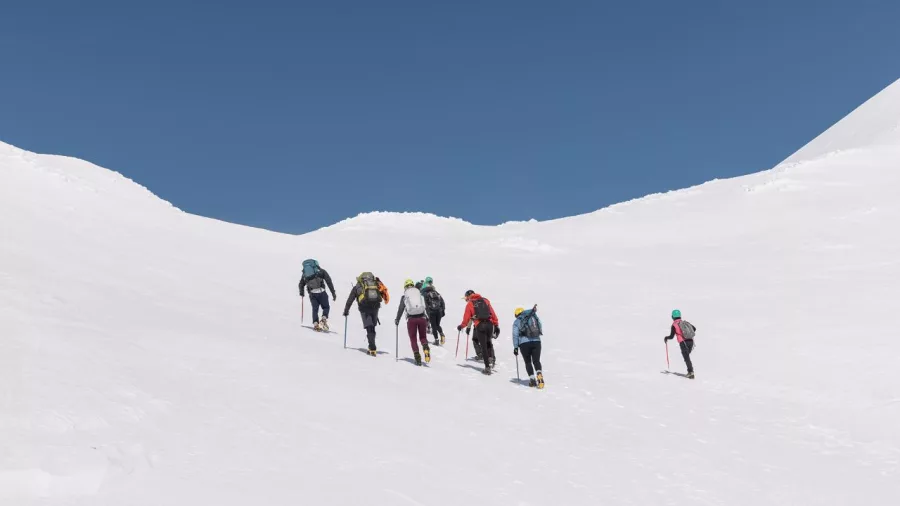 Hikers ascending a steep snow-covered ridge on Mount Ruapehu under a clear blue sky