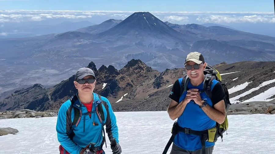 Two hikers on Mount Ruapehu with dramatic volcanic peaks and Mount Ngauruhoe in the background