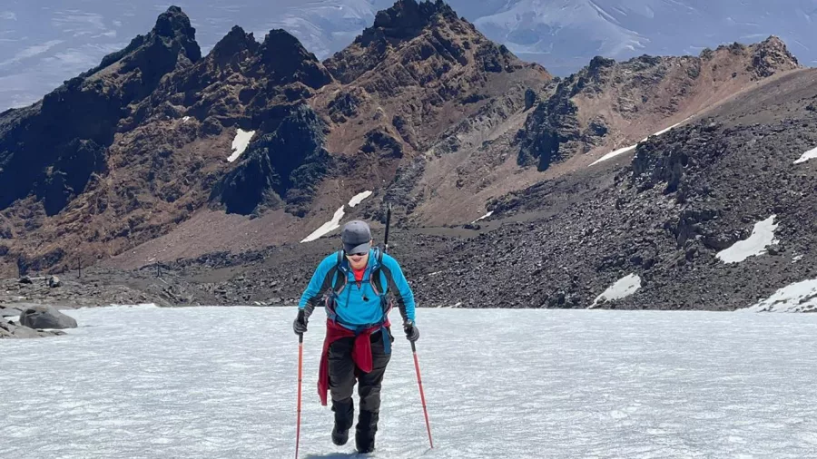 Solo climber ascending icy slopes on Mount Ruapehu with volcanic ridgelines behind