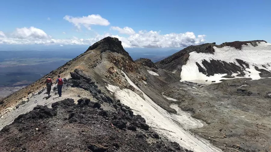 Hikers walking along the rocky and snow-dusted crater ridge on Mount Ruapehu in summer