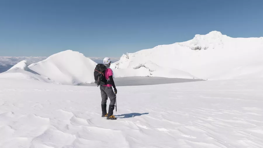 Solo hiker in crampons overlooking the snowy crater lake on Mt Ruapehu Summit Plateau
