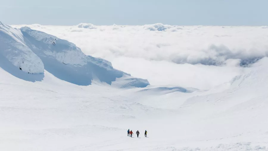 Small group hiking in deep snow on Mt Ruapehu surrounded by clouds and snow-covered ridges