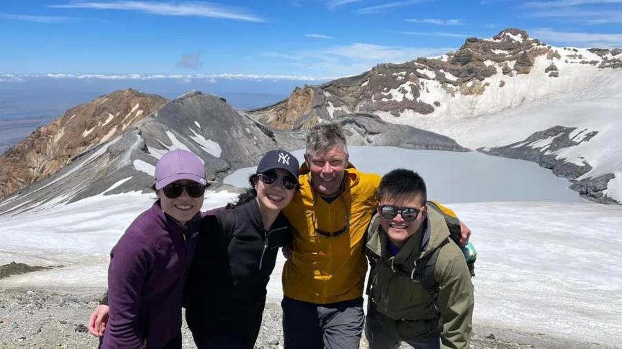 Guided group smiling at the summit of Mount Ruapehu with crater lake and volcanic terrain behind