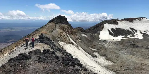 Hikers walking along the rocky and snow-dusted crater ridge on Mount Ruapehu in summer