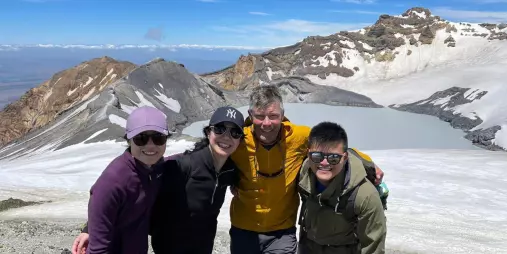 Guided group smiling at the summit of Mount Ruapehu with crater lake and volcanic terrain behind