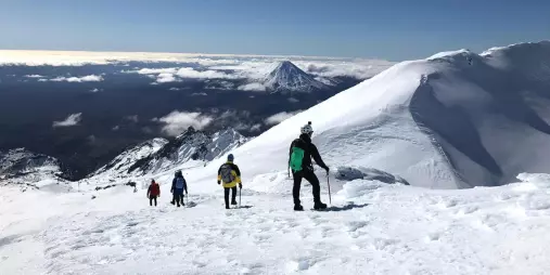 Guided hikers descending Mt Ruapehu’s snowy summit with panoramic views of Mount Ngauruhoe