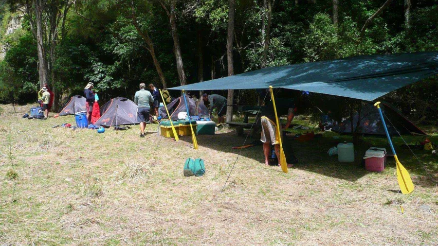 Tents and a covered dining area set up at a grassy campsite beside native bush on the Rangitikei River