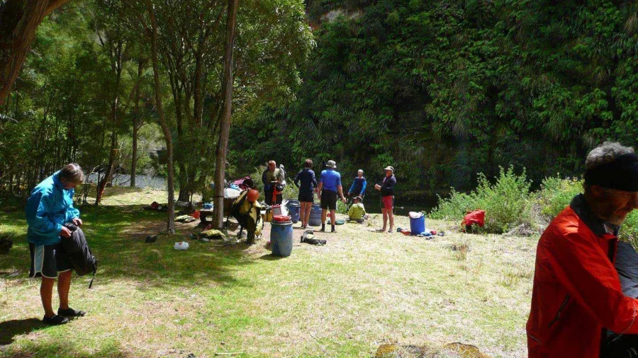 Group of paddlers setting up camp beside the Rangitikei River with trees and steep cliffs in the background