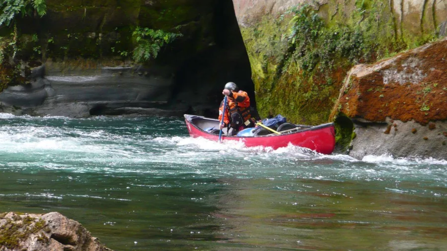 Two people navigating through a steep papa gorge in a red canoe on the Rangitikei River