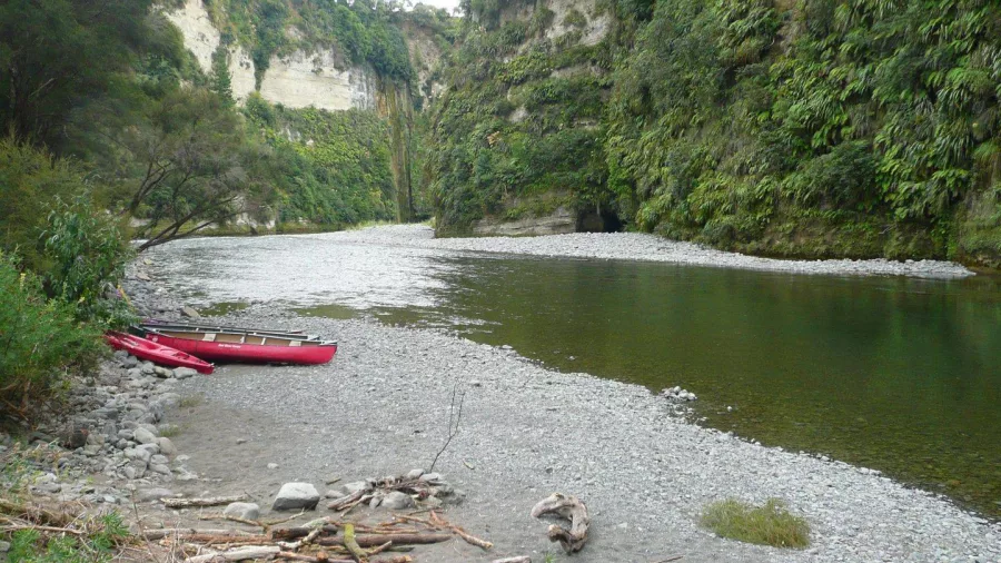 Canoes pulled up on a pebbled riverbank beside steep papa cliffs along the Rangitikei River