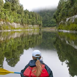 Solo paddler canoeing down the calm Whanganui River with mist and forest reflections