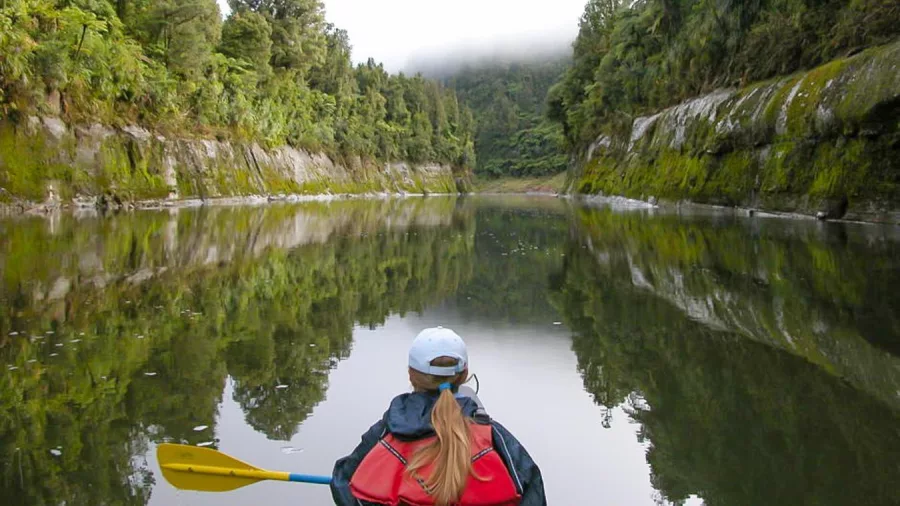 Solo paddler canoeing down the calm Whanganui River with mist and forest reflections