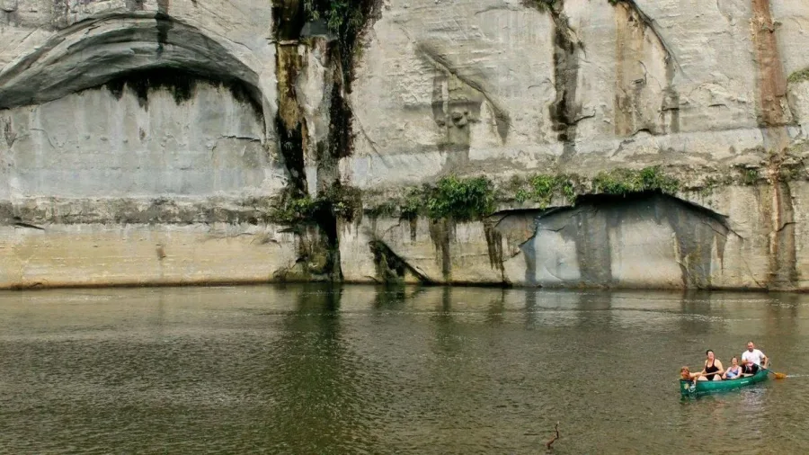 Family paddling a canoe past towering sandstone cliffs on the Whanganui River