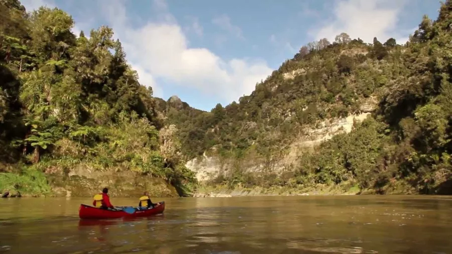 Two people paddling a red canoe along a cliff-lined stretch of the Whanganui River