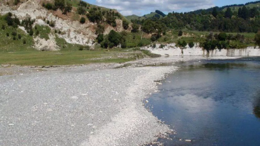 Canoes resting on a gravel bank beside the Whanganui River under a blue sky