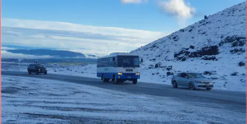 Vehicles including a ski shuttle bus driving along a snow-covered road between Ohakune and Turoa Ski Area