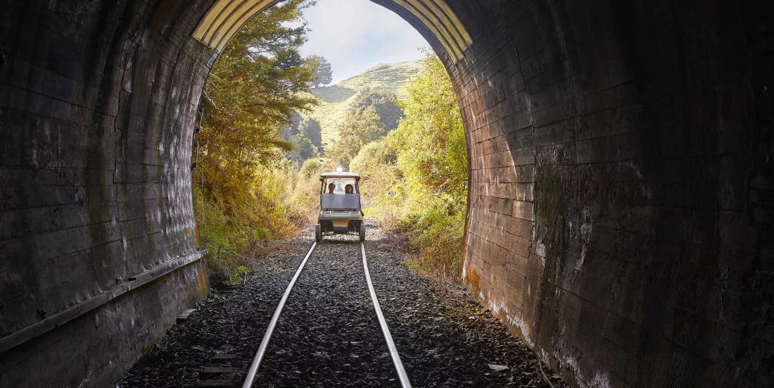 Rail cart exiting a dark tunnel into sunlit hills on the Forgotten World Adventures rail trail.