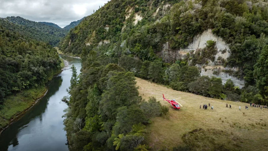 Helicopter landing beside a remote river valley surrounded by forested cliffs on the Expedition tour.