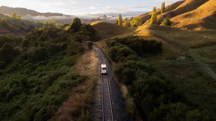 Rail cart travelling through remote hill country with golden light and mist in the distance.