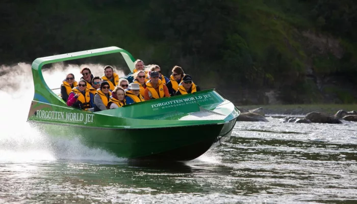 Front-facing shot of a green jet boat filled with smiling passengers on a river journey.