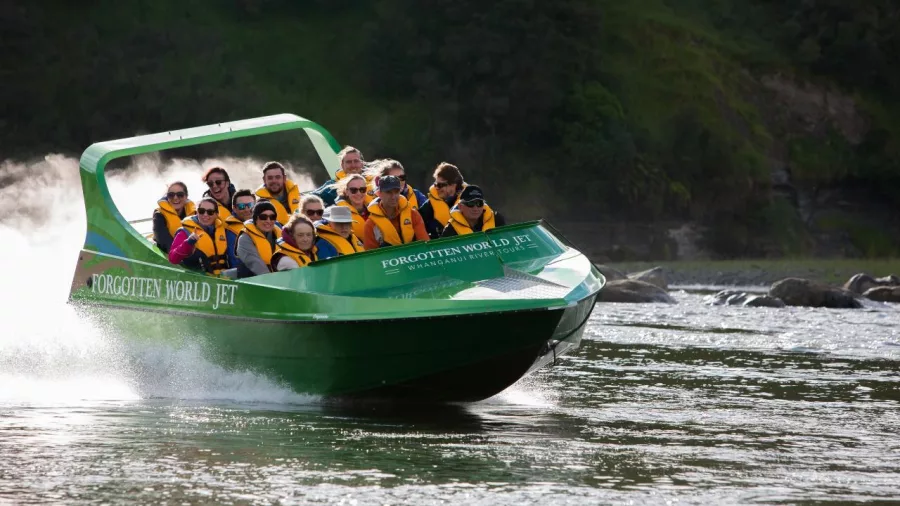 Front-facing shot of a green jet boat filled with smiling passengers on a river journey.