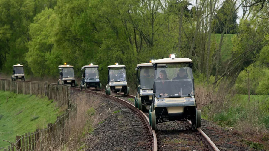 Multiple rail carts travel together along a curved railway track lined with greenery.