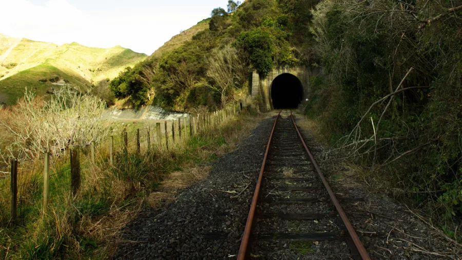 Railway track curving gently into a dark tunnel surrounded by hills and fences.