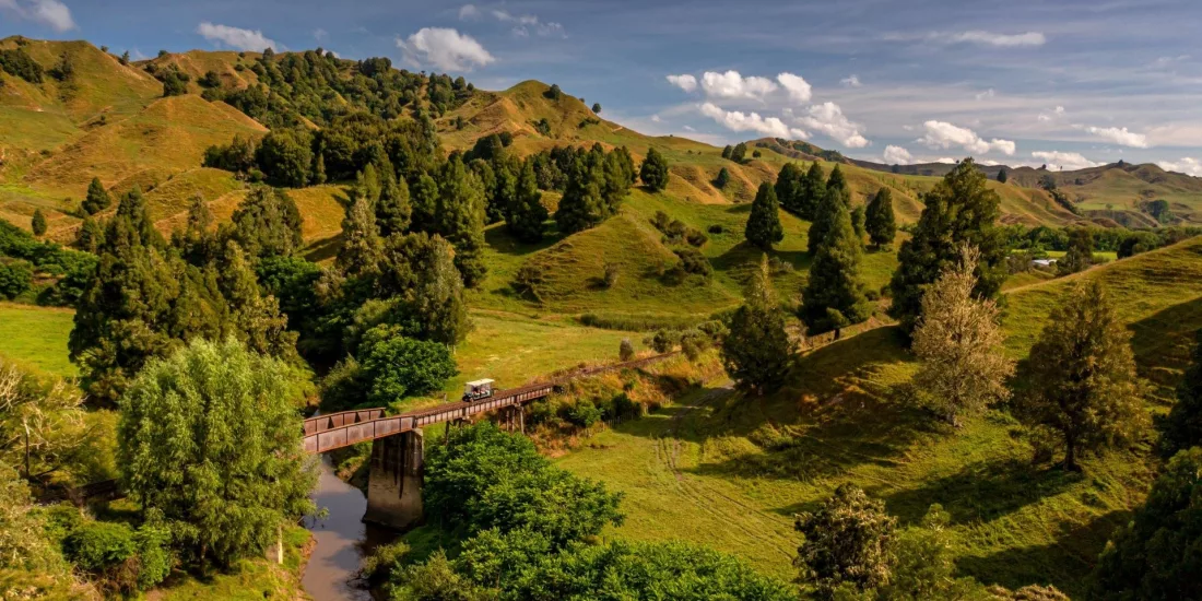 Rail cart crossing a narrow bridge through rolling green hill country on the Forgotten World Adventures rail trail.