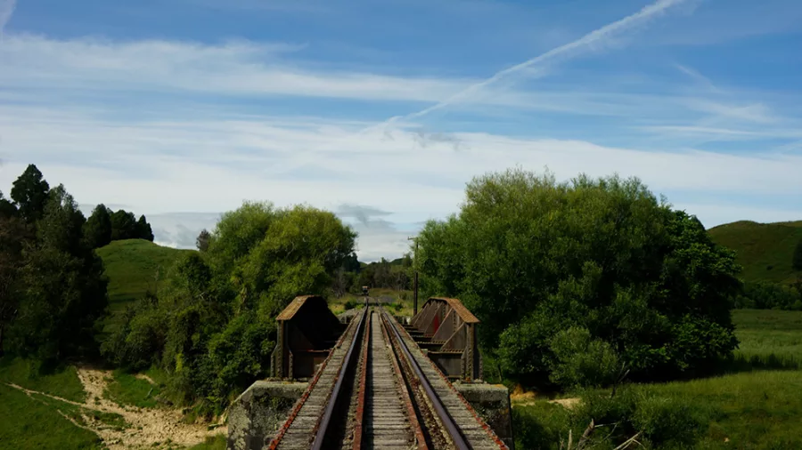 Old railway bridge crossing a river and grassy fields on the Forgotten World Adventures trail.