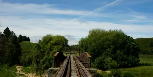 Old railway bridge crossing a river and grassy fields on the Forgotten World Adventures trail.