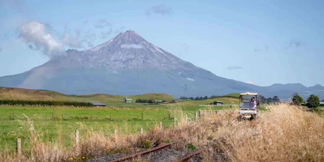 Rail cart travelling through open farmland with Mount Taranaki towering in the background.