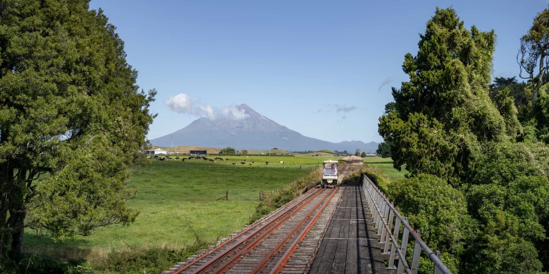 Rail cart crossing a bridge with Mount Taranaki in the distance on the Forgotten World Adventures tour.