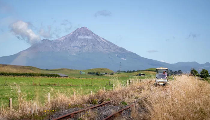 Rail cart travelling through open farmland with Mount Taranaki towering in the background.