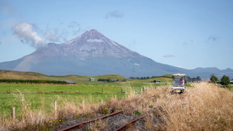 Rail cart travelling through open farmland with Mount Taranaki towering in the background.