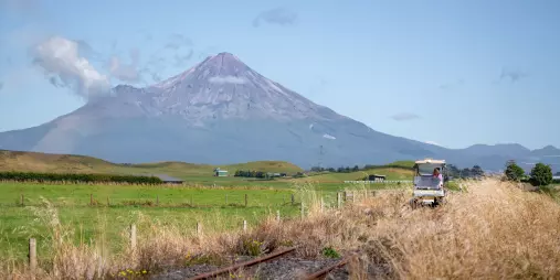 Rail cart travelling through open farmland with Mount Taranaki towering in the background.