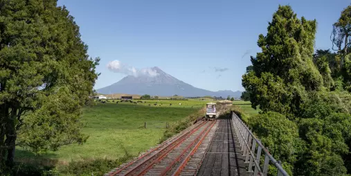 Rail cart crossing a bridge with Mount Taranaki in the distance on the Forgotten World Adventures tour.