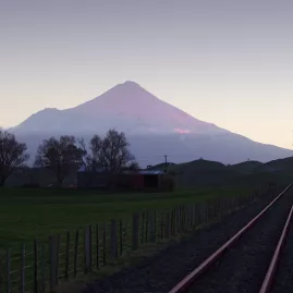 Railway tracks leading toward a distant Mount Taranaki under a purple dusk sky.